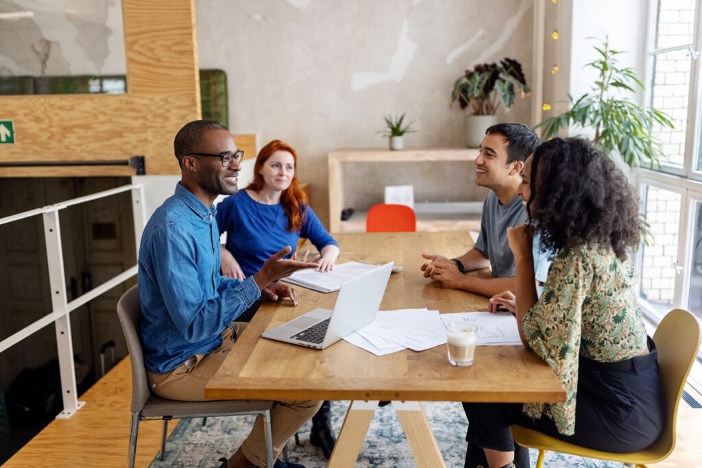 Multiracial business people discussing in office meeting. Male and female professionals sitting at conference table brainstorming on new project.