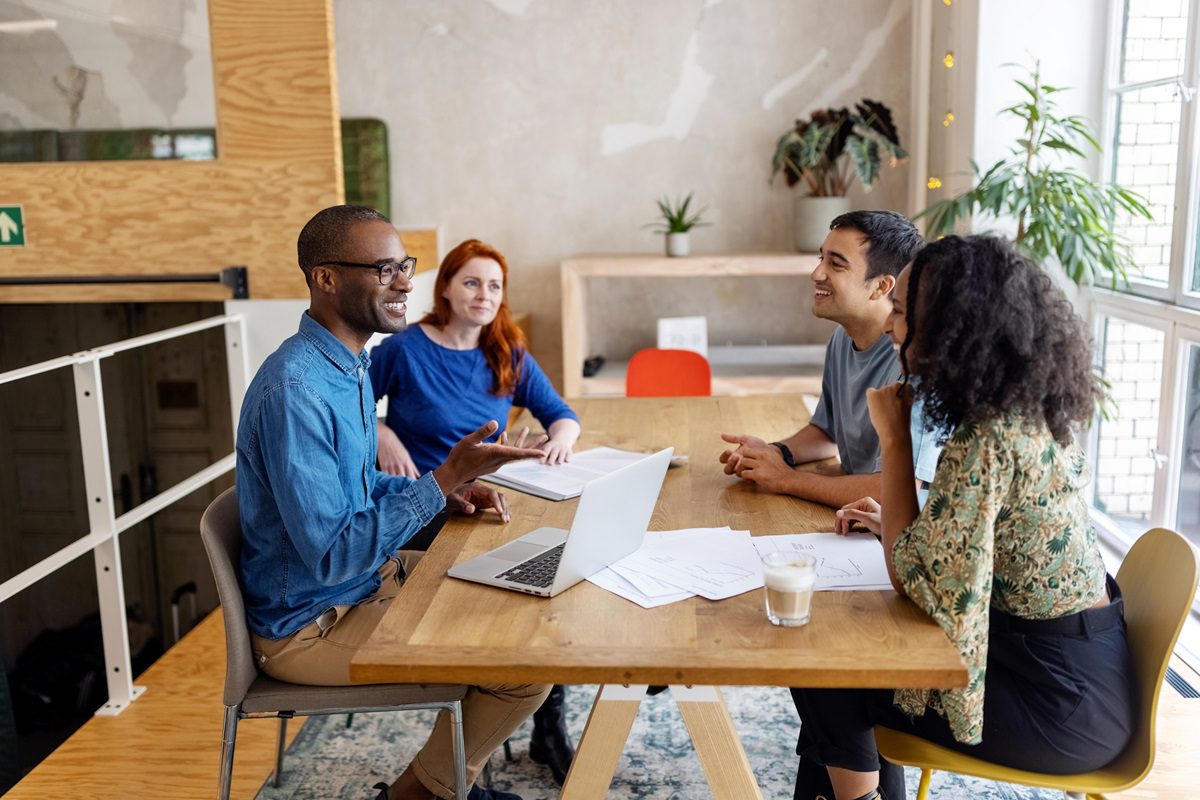 Multiracial business people discussing in office meeting. Male and female professionals sitting at conference table brainstorming on new project.