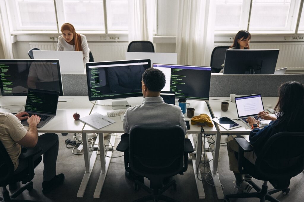 High angle view of male and female tech professionals working on computers and laptops while sitting at desk in office