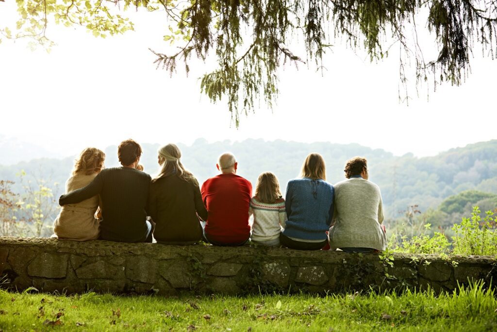 Rear view of multi-generation family relaxing in row on retaining wall against clear sky