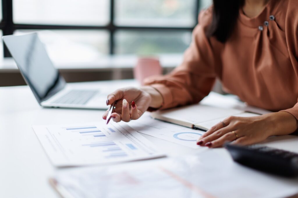 Woman analyzing financial data on business reports. Holding a pen over charts and graphs. Working with a laptop and calculator on an office desk. Illustrating concepts of finance. Accounting