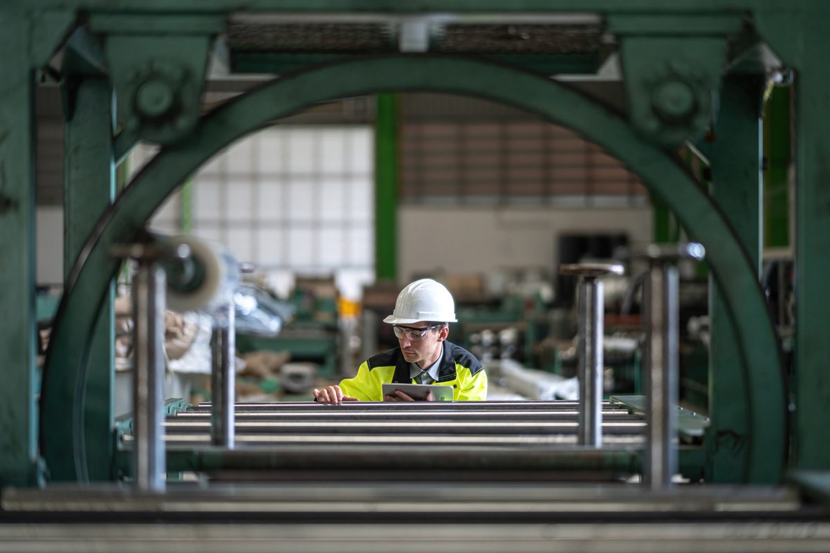 Male engineer and tablet working at manufacturing factory. Close-up of engineer Male using yoke machine. Male engineer is wearing protective glasses in factory.
