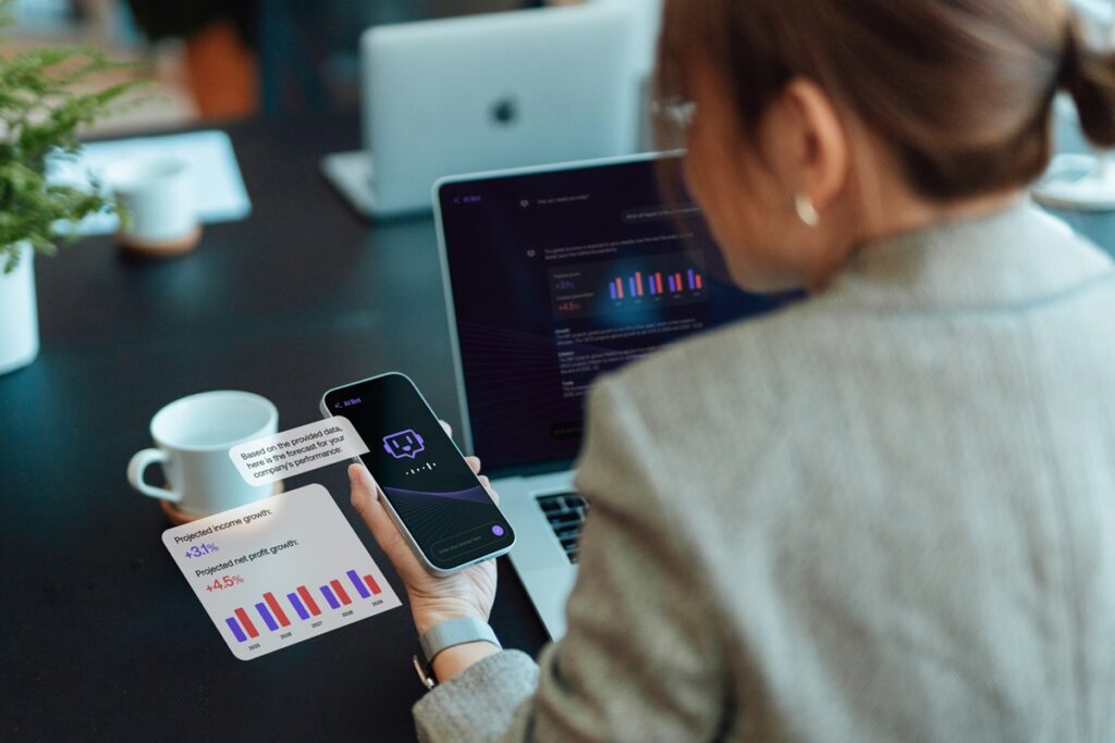 Over the shoulder view of businesswoman talking to virtual assistance on smartphone, using AI chatbot to generate information and analyse data. Open AI technology. Online robot system. Business and technology.