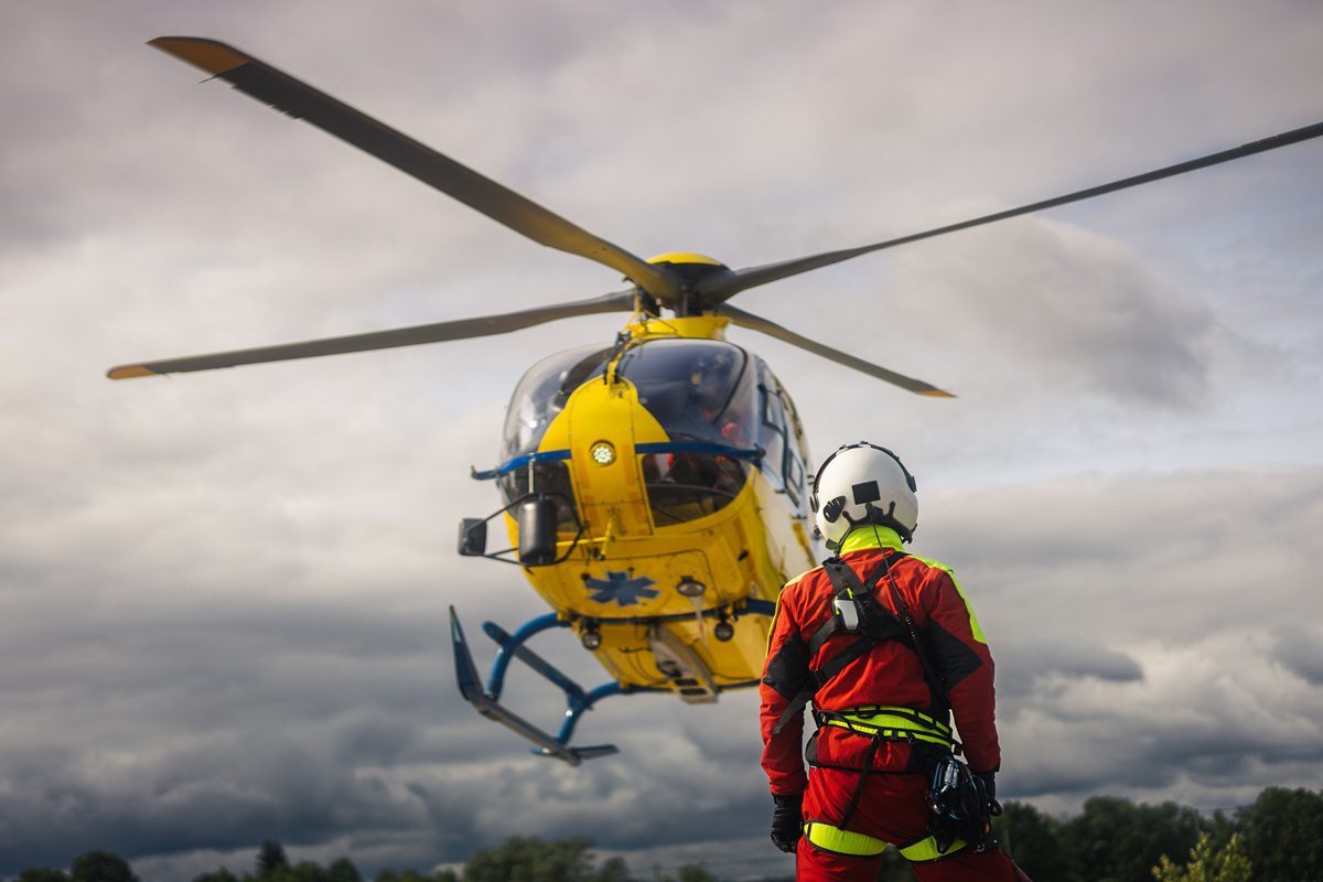 Rear view of paramedic in helmet looking at medical helicopter landing. Air rescue, emergency medical response, healthcare, coordination, and professional rescue operations concept.