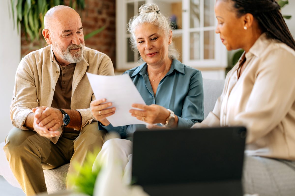 A financial advisor meets with a mature couple in their home, reviewing documents together. The atmosphere is collaborative and warm.