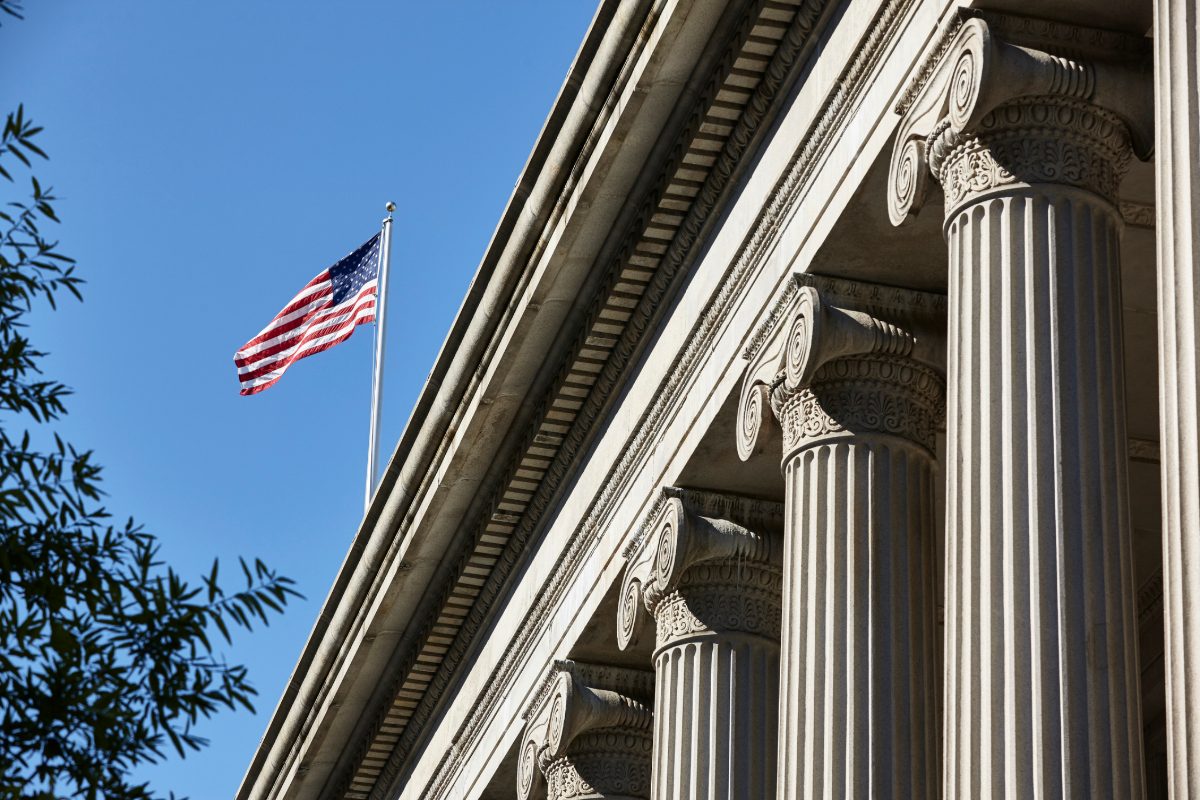 The US flag waving in the sunshine over the columns of the Treasury Departments East facade