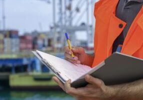 The foreman of the seaport is engaged in the reception and verification of cargo. He is holding a folder with documents in his hands.