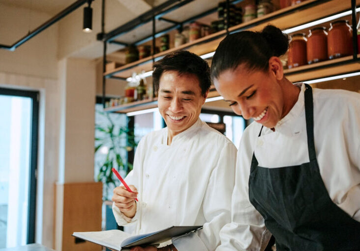 Male and female chef laughing while taking inventory in commercial kitchen - stock photo