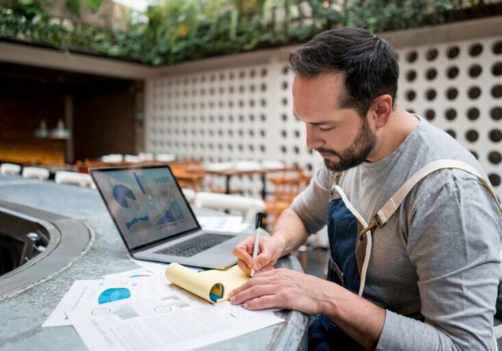 Portrait of a male business owner doing the books at a restaurant using a laptop computer
