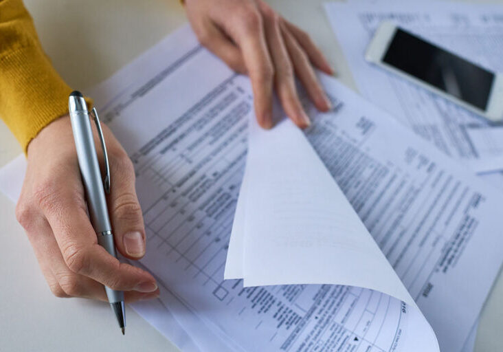Close-up of unrecognizable woman attentively examining business documents and making correction at table