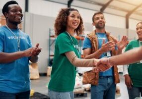 Applause, handshake and support with volunteer team in warehouse together for aid, community or welfare. Agreement, charity and donation with people shaking hands for ngo or non profit success