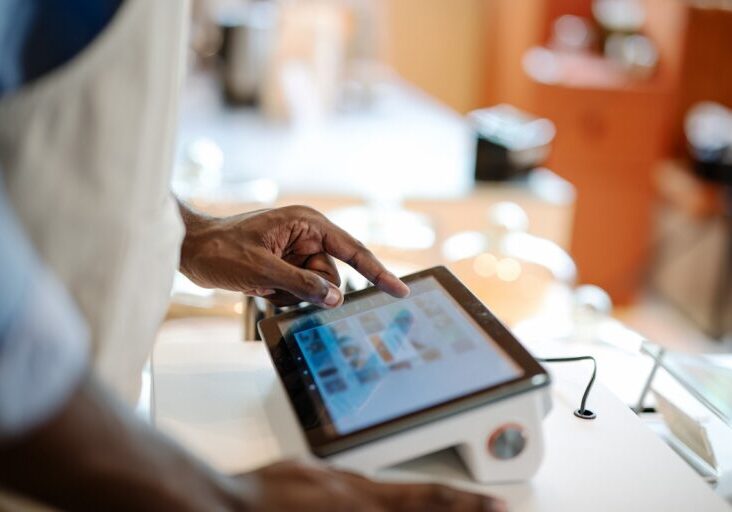Accurate, Real-time Data and Faster Speed of Service Can Invest in a POS System in Your Store. Close-up of a male African-American cashier placing orders via a point of sale (POS) software at a cashier counter of a coffee shop.