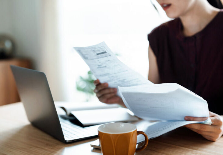 Cropped shot of Asian woman sitting at dining table, handling personal finance with laptop.
