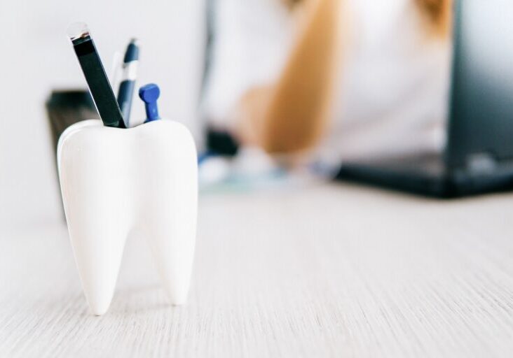 Tooth shaped pencil holder on desk - dentist with laptop on background