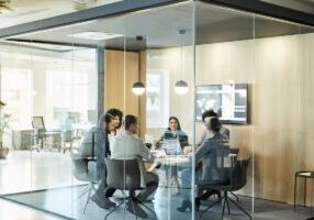 Business colleagues sitting at conference table seen through glass wall. Multi-ethnic coworkers are discussing in board room at office. They are planning strategy.