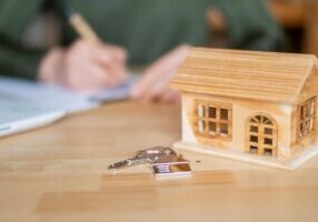 Real estate agent signing a contract for a new home purchase, accompanied by a small wooden house model and keys resting on the table, symbolizes success in the housing market - stock photo