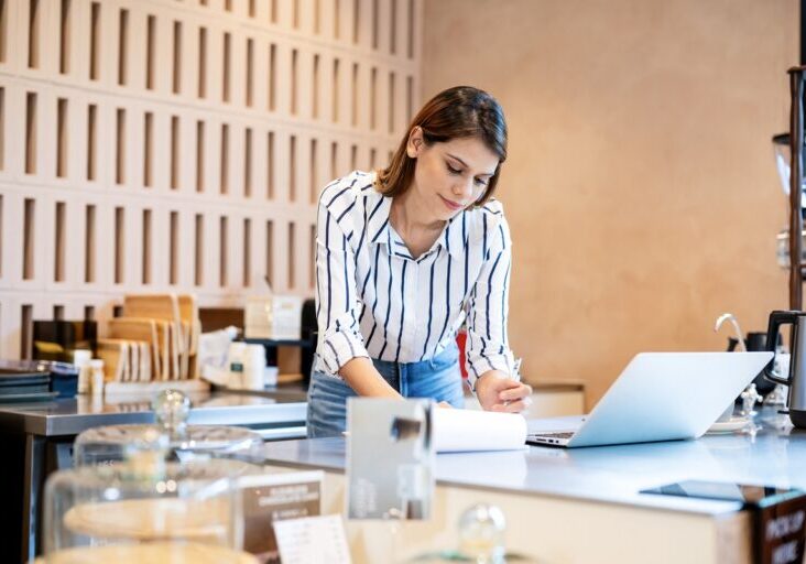 Coffee Shop and Restaurants Rewards Program Strategy Can Be a Fulfilling Demanding Experience. A female coffee shop owner uses a laptop computer to do business and marketing strategies to increase customers and sales in her coffee shop. - stock photo