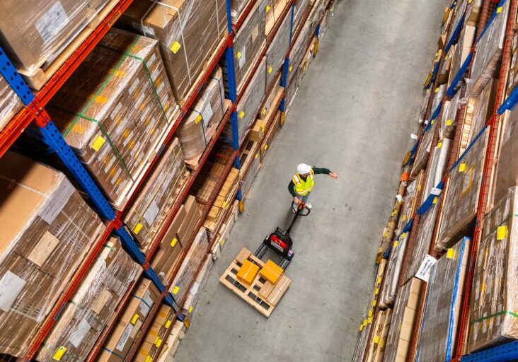 Top-Down View: In Warehouse People Working, Forklift Truck Operator Lifts Pallet with Cardboard Box - stock photo