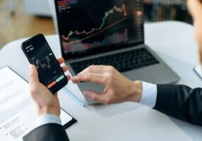 Successful male crypto trader, investor, using a laptop and smartphone, analyzes trading charts in the stock market of a digital cryptocurrency exchange, analyzes, buys and sells cryptocurrencies