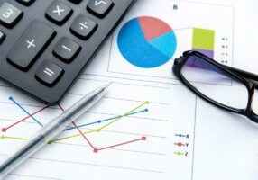 Closeup view of business graphs, ballpoint pen, calculator and glasses on desk.