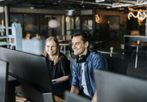 Happy male and female entrepreneurs watching computer screen sitting in tech startup office