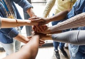 Close up shot of unrecognizable group of diverse individuals forming a united front, holding their hands stacked in a gesture of solidarity.