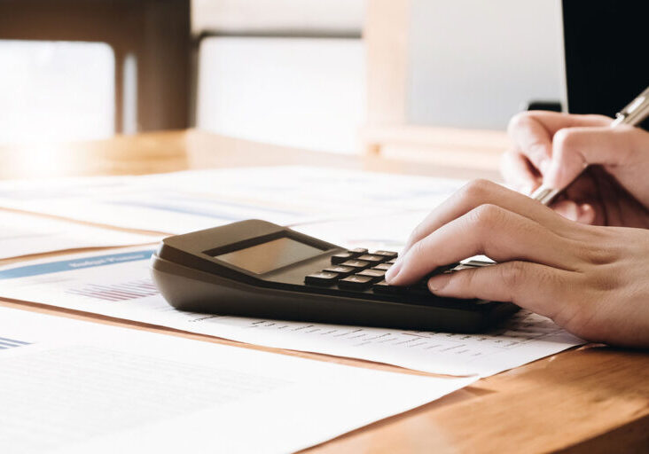 Close up of businesswoman or accountant hand holding pen working on calculator to calculate business data, accountancy document and laptop computer at office, business concept