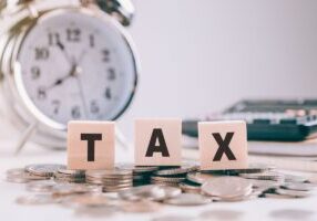 Tax Concept.Word wooden block on coins and Clock with calculator