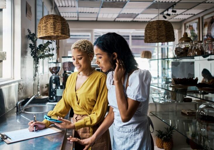 Small business owners working together and writing down orders in a coffee shop. Female entrepreneurs in partnership collaborating, brainstorming and planning sales for their cafe