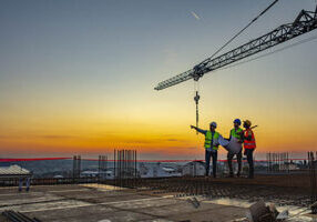 construction workers by crane at sunset