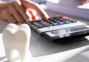 model of tooth and a male hand entering computation on desk calculator