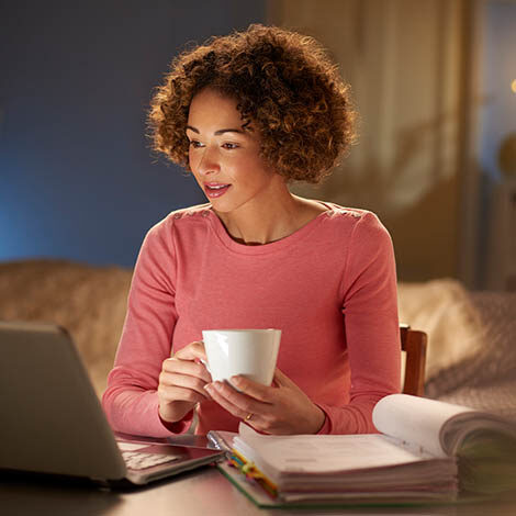 a young woman works at home at night , going through her paperwork and bills .she is working at her laptop . She could be running her own business or returning to part time education .